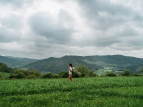 Ein sanfter Wind streicht über die weiten Wiesen, während die Wolken über die majestätischen Berge ziehen. Die Wanderin genießt die frische Luft und die atemberaubende Aussicht, die die Natur hier bietet. Ein perfekter Ort, um die Seele baumeln zu lassen und die Schönheit der Landschaft zu erleben.