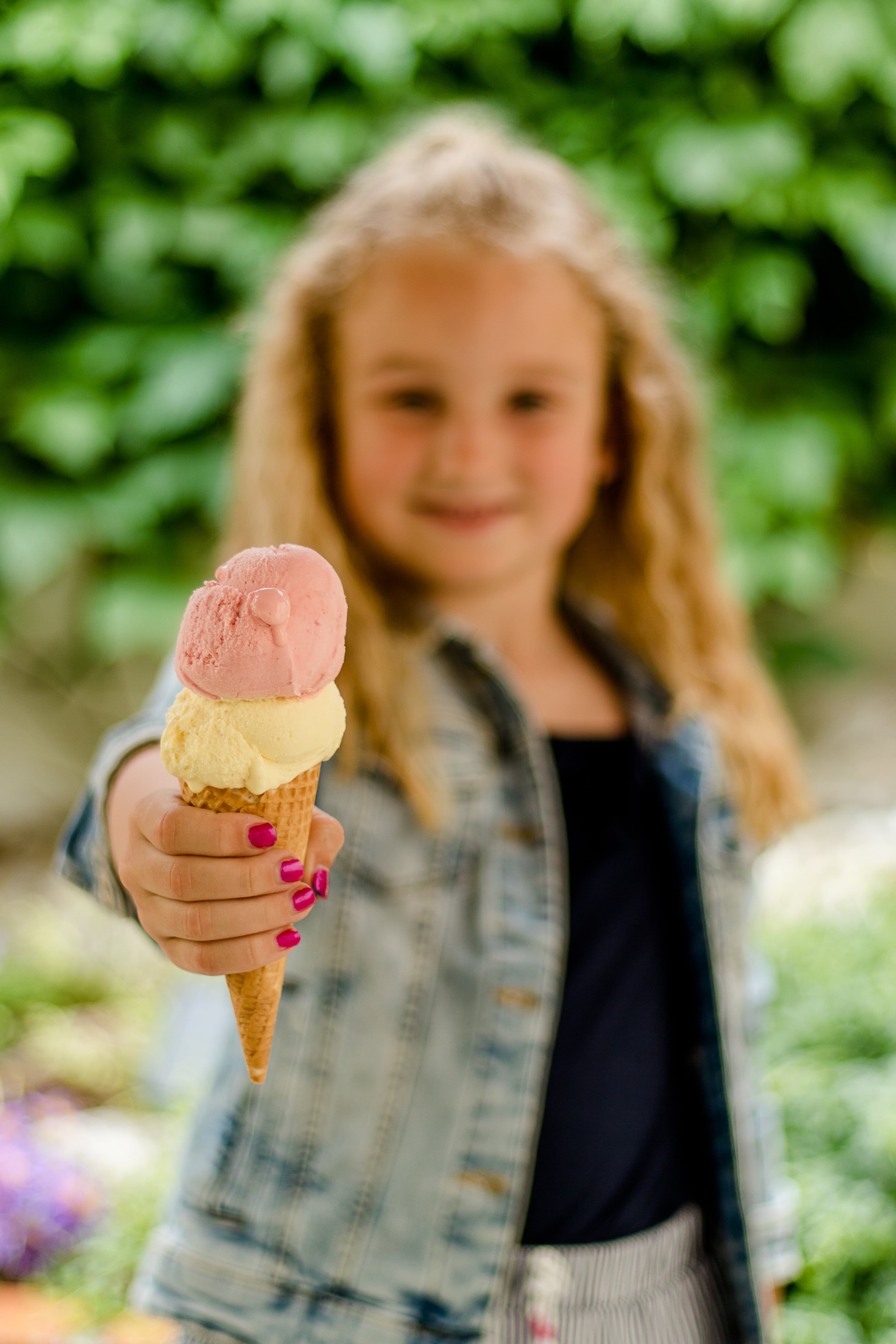 Ein Kind hält eine Eistüte mit zwei Kugeln, eine rosa und eine gelbe, in der Hand.