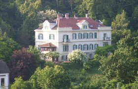 Großes, weißes Gebäude im Grünen, umgeben von Bäumen.