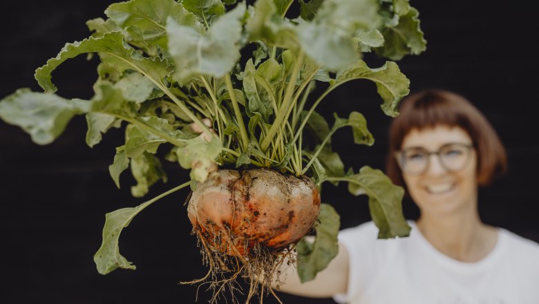 Frau hält große Rübe mit Blättern in der Hand.