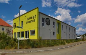 Außenansicht eines modernen, zweistöckigen Motels mit gelber Fassade und der Aufschrift 'Einfach gut übernachten'.