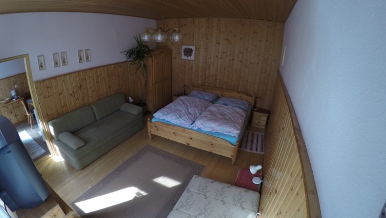 Ein gem&uuml;tliches Schlafzimmer mit Holzw&auml;nden, einem Doppelbett, einem Sofa und einem Teppich auf Holzboden.