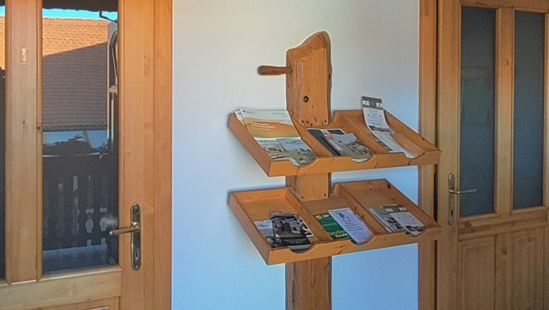 Ein Holzregal mit Prospekten an einer wei&szlig;en Wand zwischen zwei Holzt&uuml;ren.