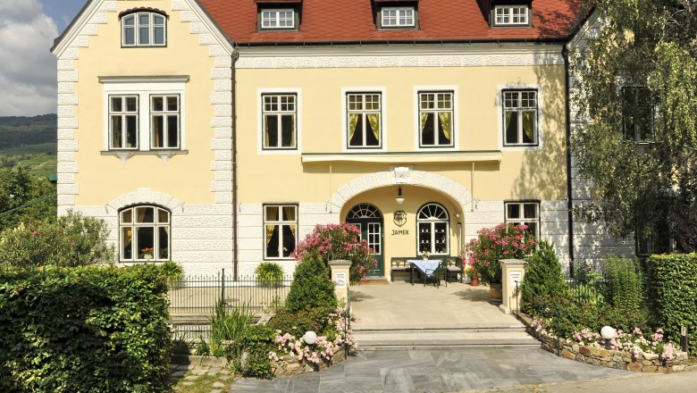 Gelbes Gebäude mit rotem Dach und Garten, Weingut Josef Jamek.