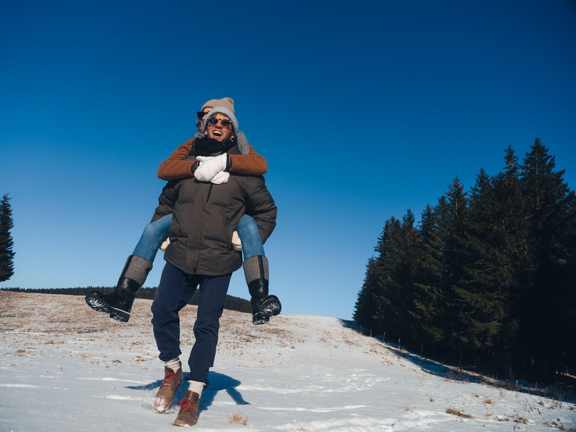 In der winterlichen Landschaft der Wiener Alpen genießen zwei Freunde die frische Luft und die schneebedeckte Natur. Lachen und Freude erfüllen die kalte Umgebung, während sie gemeinsam die Schönheit der winterlichen Wanderung erleben.