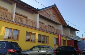 Außenansicht eines gelben Gebäudes mit Holzveranda und Autos davor.