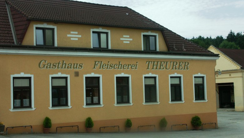 Au&szlig;enansicht des Gasthauses und der Fleischerei Theurer mit gelber Fassade und braunem Dach.