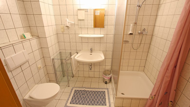 Kleines Badezimmer mit Dusche, Waschbecken und Toilette, gefliest in Wei&szlig;.