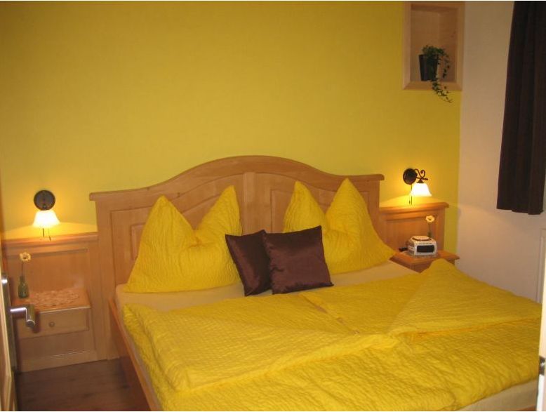 Gemütliches Gästezimmer mit gelber Bettwäsche und Holzmöbeln.