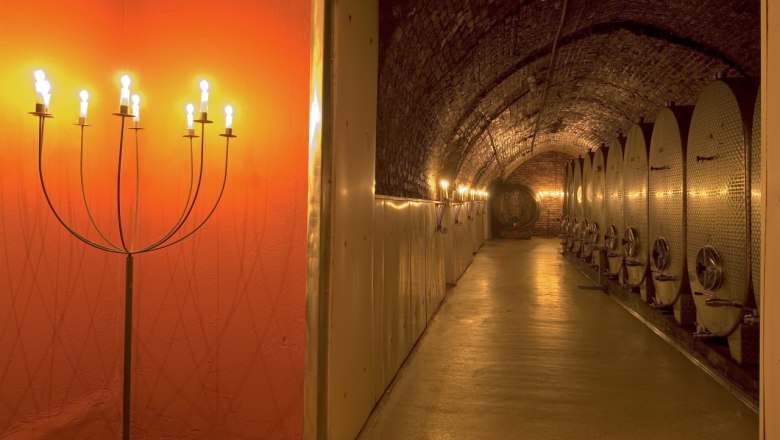 Weinkeller mit beleuchteten Metalltanks und Kerzenleuchtern.