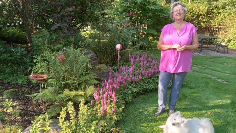 Eine Frau steht in einem Garten neben einem wei&szlig;en Hund auf dem Rasen.