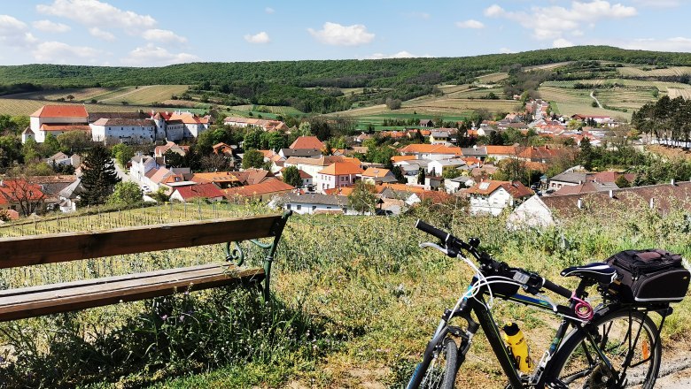 Fahrrad und Bank mit Blick auf ein Dorf in h&uuml;geliger Landschaft.