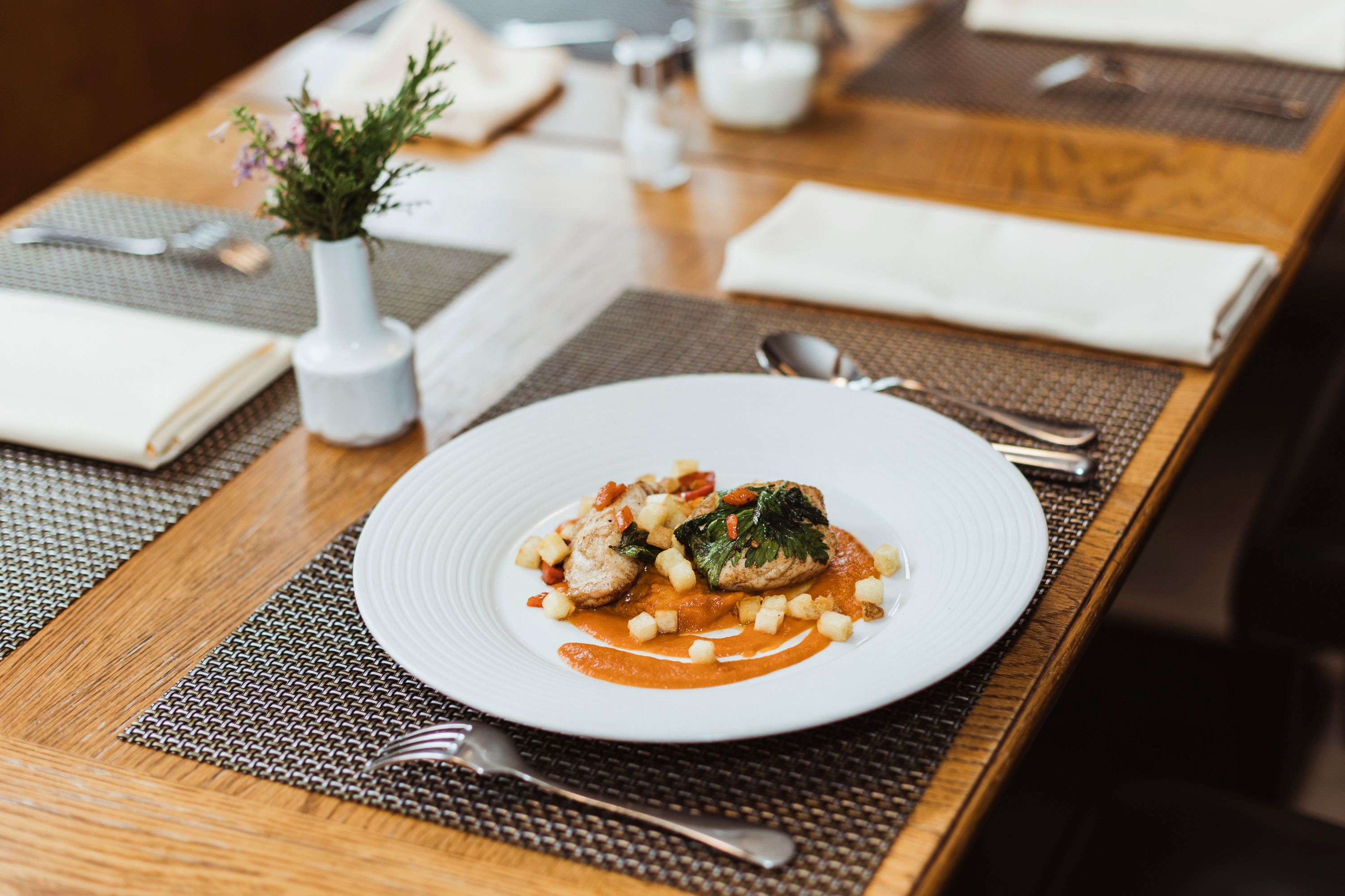 Elegantes Gericht auf weißem Teller, dekorativ angerichtet auf Holztisch.