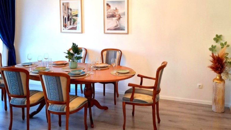 Esszimmer mit ovalem Holztisch, sechs St&uuml;hlen, zwei Wandbildern und Dekorationen.