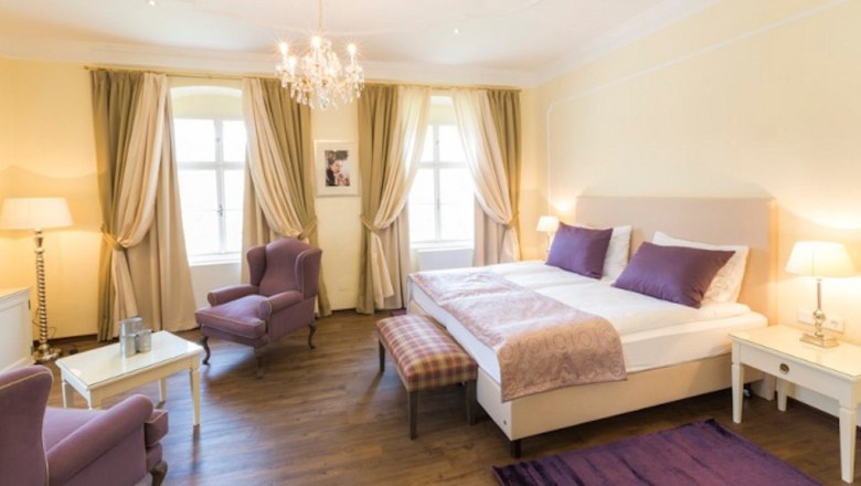 Elegantes Schlafzimmer mit Doppelbett, lila Akzenten und Kronleuchter.