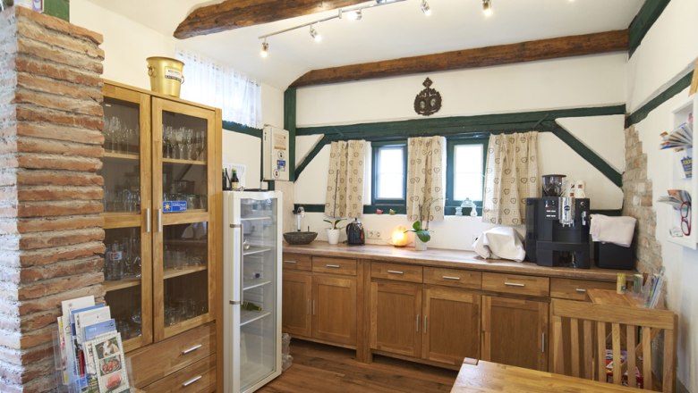 Ein gem&uuml;tlicher Fr&uuml;hst&uuml;cksraum mit Holzm&ouml;beln, einem K&uuml;hlschrank, einer Kaffeemaschine und dekorativen Holzbalken an der Decke.