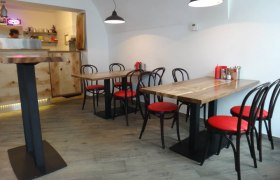 Innenansicht eines modernen Restaurants mit Holztischen und roten Stühlen.