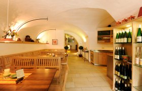 Innenansicht eines gem&uuml;tlichen Heurigenlokals mit Holztischen und Weinregalen.