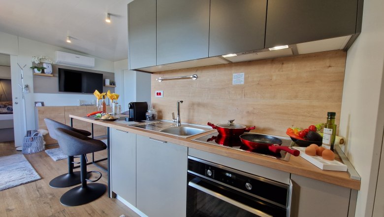 Moderne K&uuml;che mit grauen Schr&auml;nken, Herd, Sp&uuml;le und Barhockern.