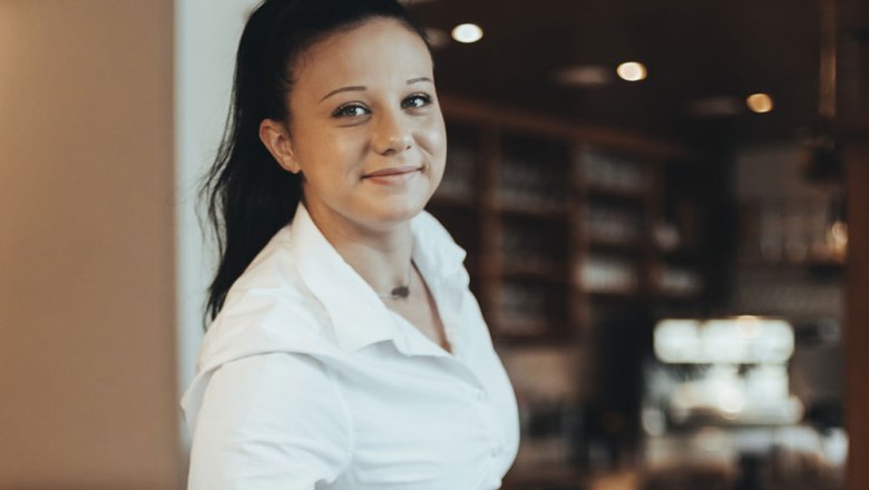 Frau in wei&szlig;em Hemd l&auml;chelt in die Kamera, Hintergrund unscharf.