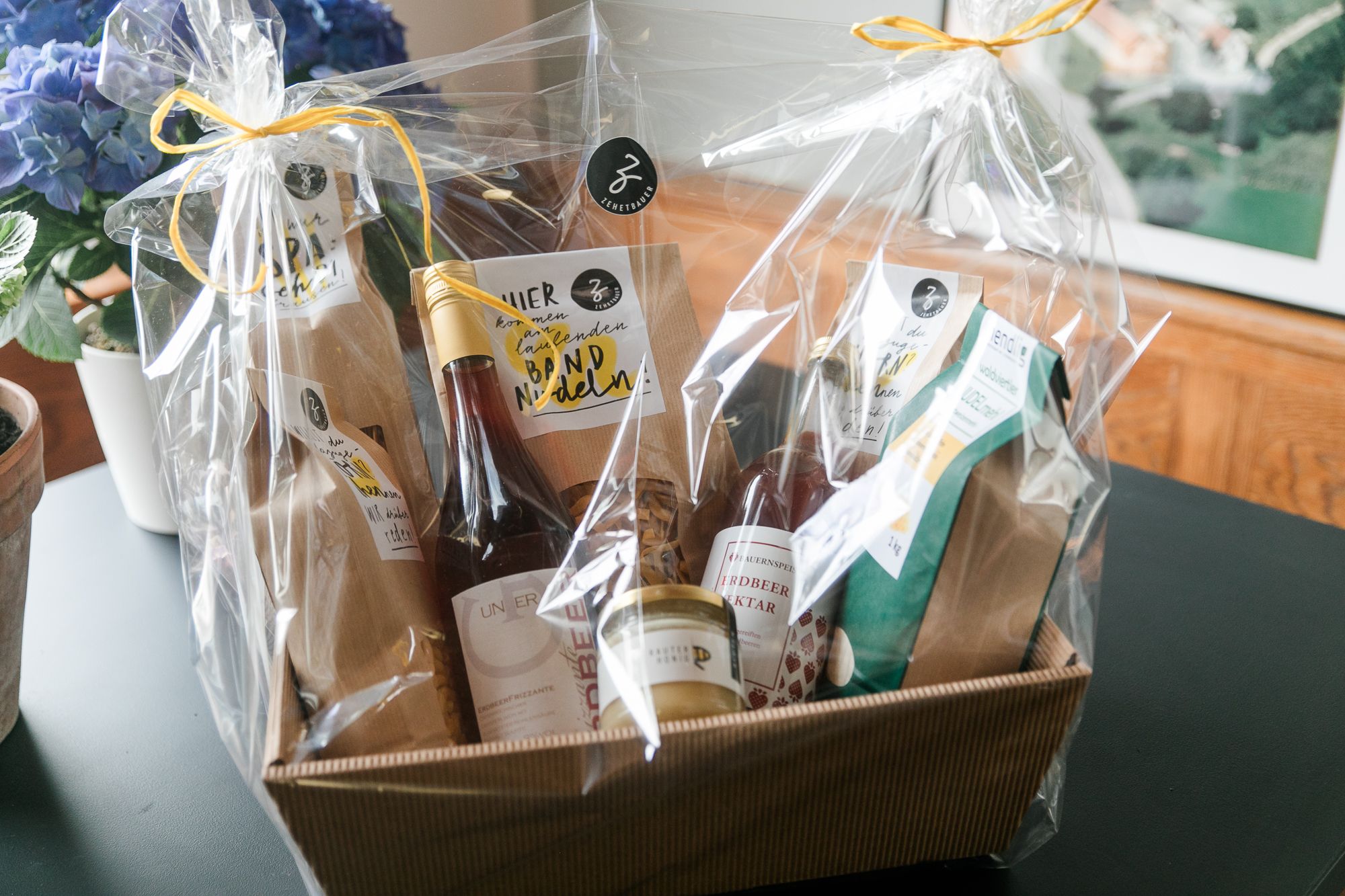 Geschenkkorb mit regionalen Produkten, verpackt in Folie, auf einem Tisch.