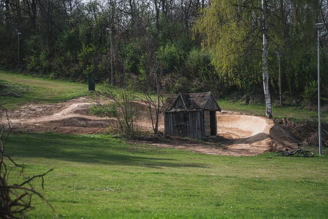 Eine Mountainbike-Strecke mit einer Holzhütte und einem Fahrrad im Vordergrund, umgeben von Bäumen und Gras.
