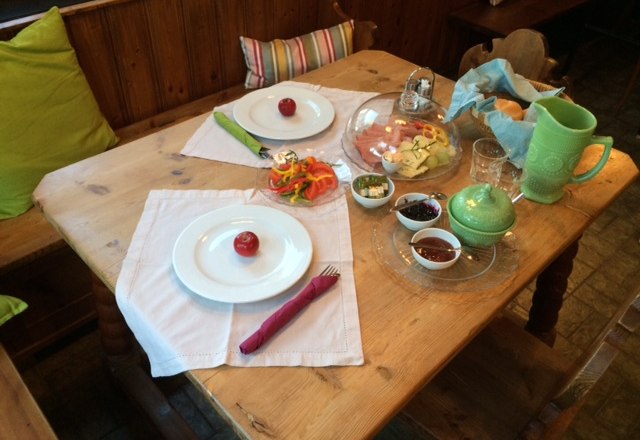 Ein gedeckter Fr&uuml;hst&uuml;ckstisch mit Tellern, Besteck, Aufschnitt, Gem&uuml;se und Getr&auml;nken.