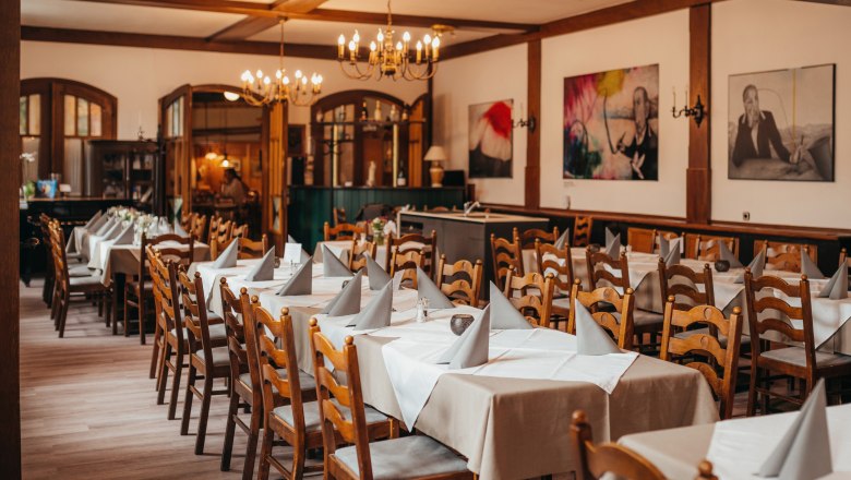 Ein gem&uuml;tlicher Speisesaal mit Holzm&ouml;beln, gedeckten Tischen und Kronleuchtern.