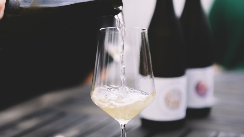 Wei&szlig;wein wird in ein Glas auf einem Tisch eingeschenkt.