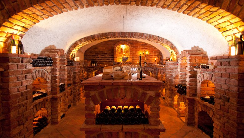 Ein stimmungsvoll beleuchteter Weinkeller mit Backsteinwänden und Weinflaschen in Regalen.