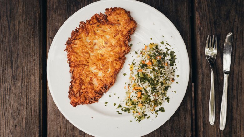 Ein Teller mit einem Kartoffel-Schnitzel und Reisgem&uuml;se auf Holztisch.