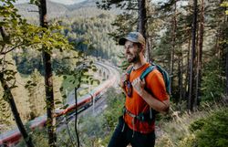 Ein Wanderer blickt auf einen Zug der gerade über ein Viadukt fährt