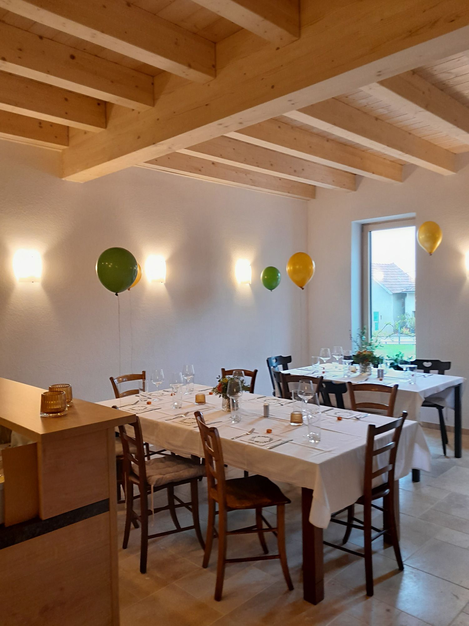 Ein festlich gedeckter Tisch in einem Raum mit Holzbalkendecke und Luftballons an der Wand.