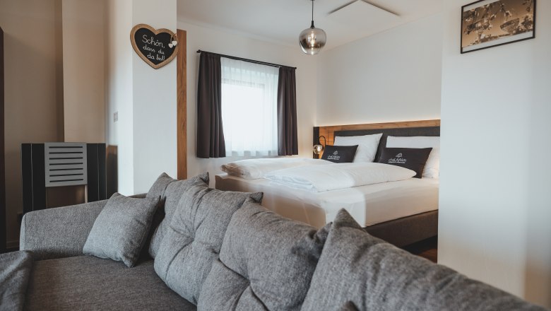 Modern eingerichtetes Schlafzimmer mit grauem Sofa und Doppelbett.