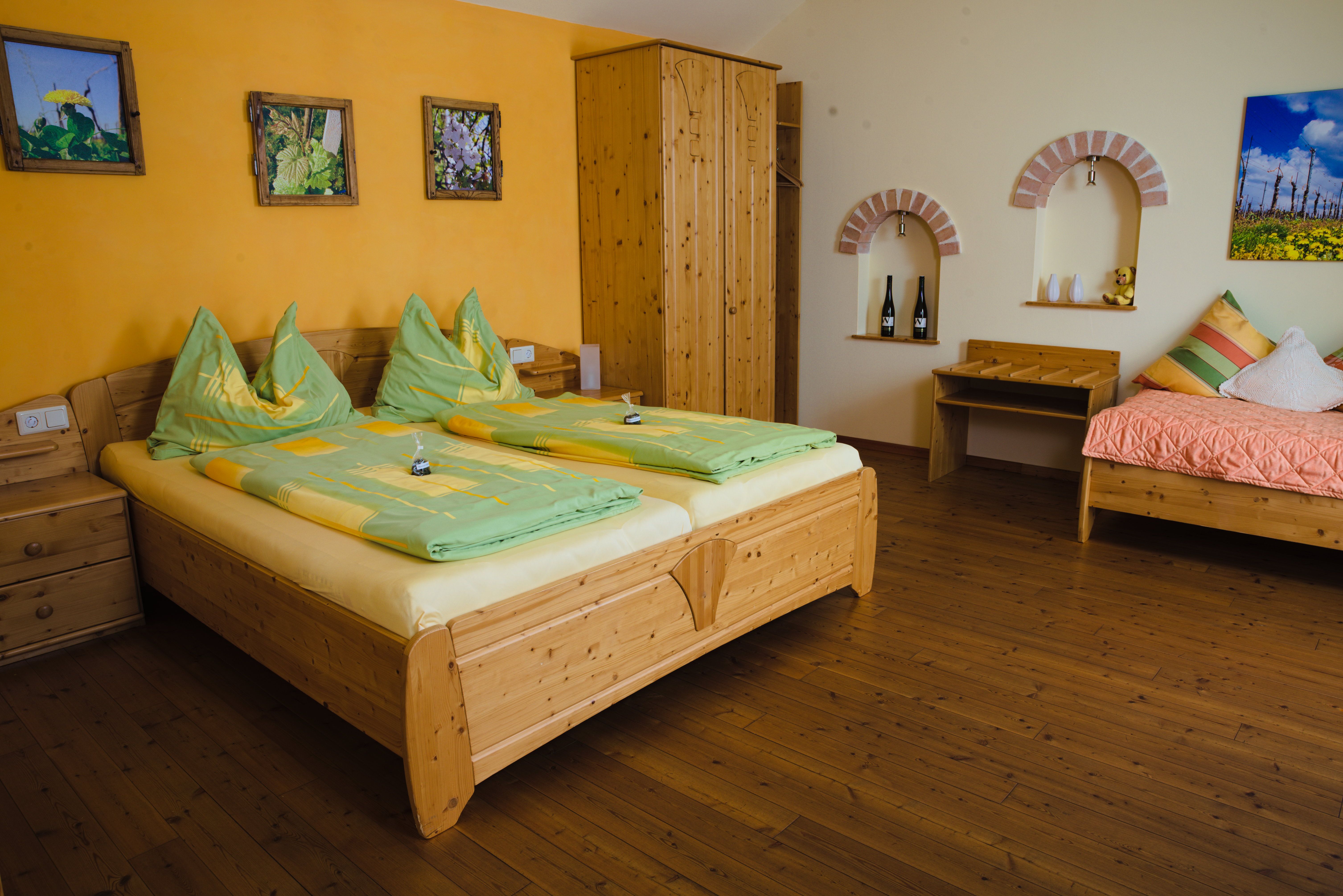 Gemütliches Gästezimmer mit Holzmöbeln, Doppelbett, Einzelbett und dekorativen Bildern an der Wand.