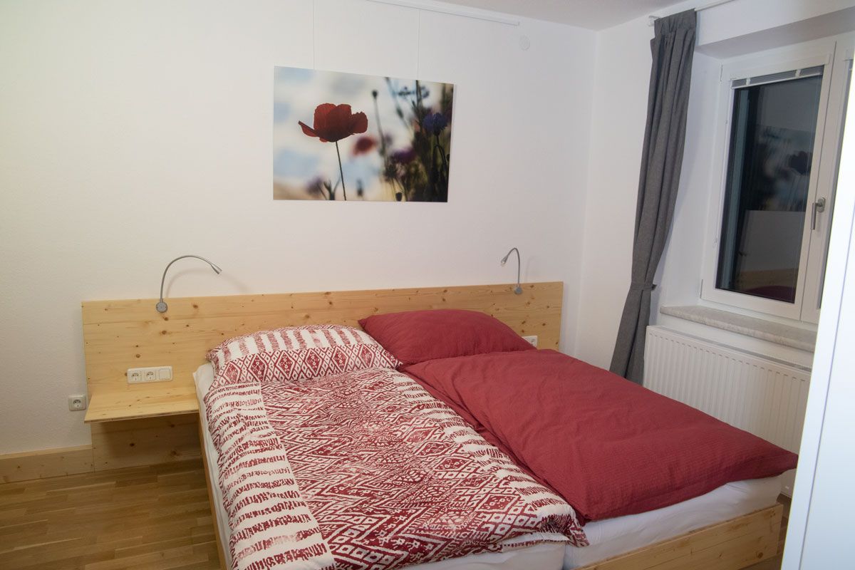 Schlafzimmer mit Doppelbett, roter Bettwäsche und einem Mohnblumenbild an der Wand.