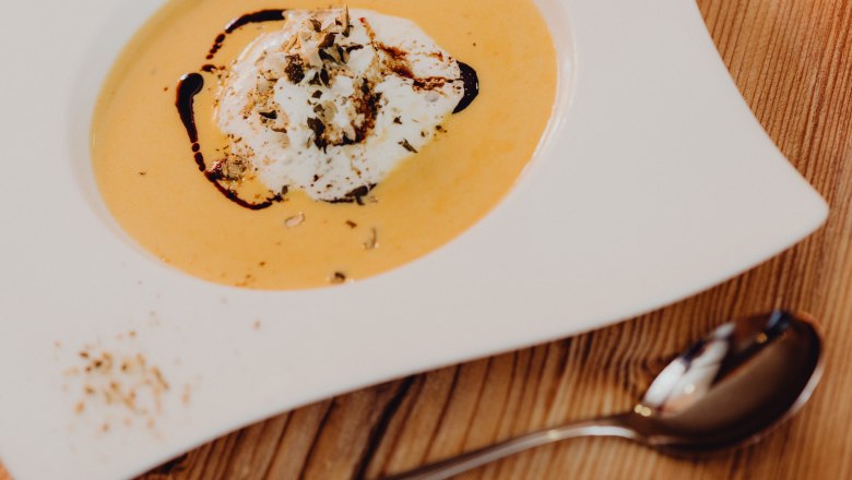 K&uuml;rbissuppe mit Sahne und K&uuml;rbiskern&ouml;l in einem wei&szlig;en Teller auf Holztisch.