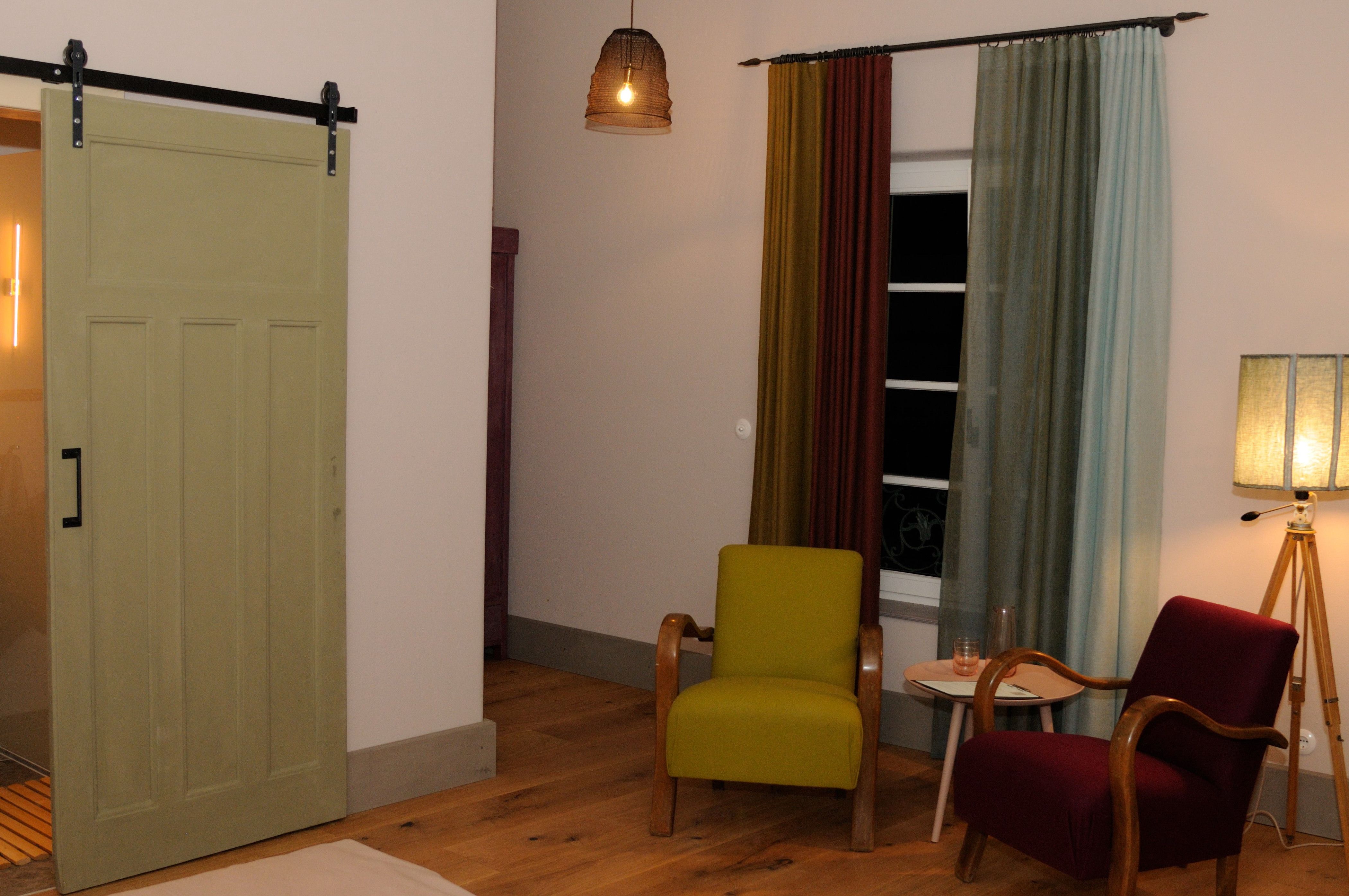 Gemütliches Zimmer mit zwei Sesseln, Vorhängen und Stehlampe.