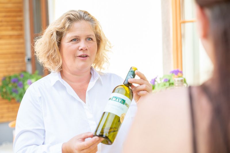 Eine Frau hält eine Weinflasche und spricht mit einer anderen Person.