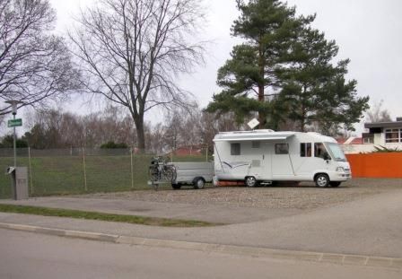 Wohnmobil auf einem Stellplatz neben einem Baum und einem Zaun.