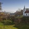 Landschaft mit Kirche und B&auml;umen bei klarem Himmel.