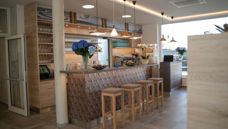 Moderne Bar mit Holzdekor, Barhockern und Blumen.