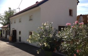 Weißes Gebäude mit roten Dachziegeln und blühenden Oleanderbüschen davor.