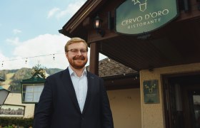 Ein Mann im Anzug steht lächelnd vor dem Restaurant Cervo D'Oro.