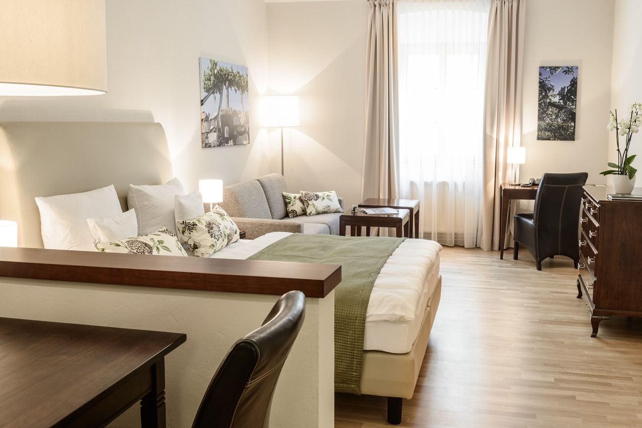 Helles, gemütliches Hotelzimmer mit Bett, Sofa, Schreibtisch und Dekoration.