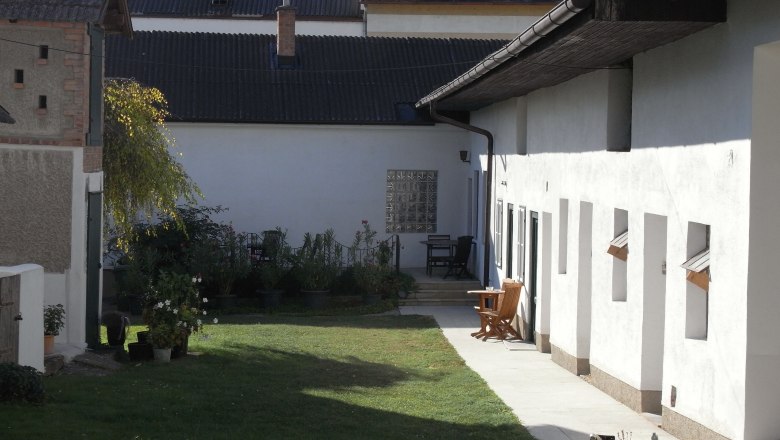 Hof mit Rasenfläche, weißen Gebäuden und Gartenmöbeln.