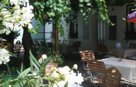 Ein gemütlicher Garten mit Holzmöbeln, weißen Blüten und Weinreben.