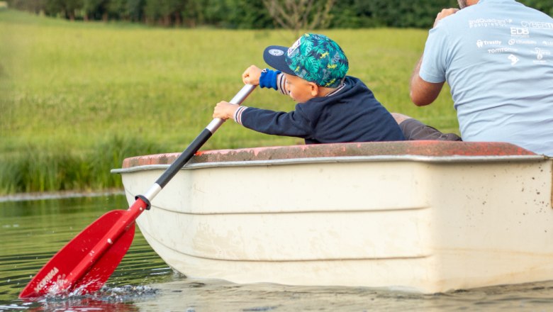 Ein Kind und ein Erwachsener rudern in einem kleinen Boot auf einem Teich.