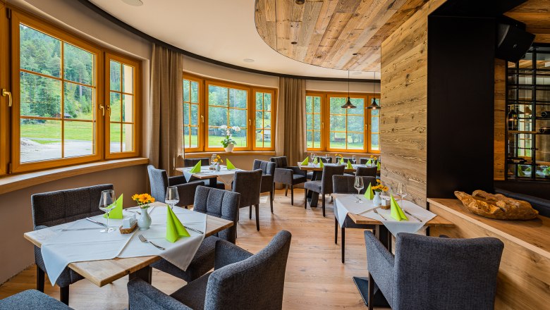 Elegantes Restaurant mit Holzelementen, gedeckten Tischen und großen Fenstern mit Blick ins Grüne.