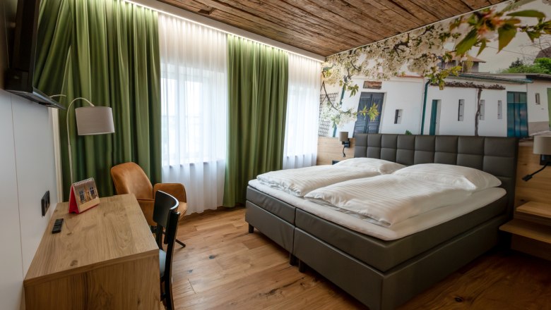 Modernes G&auml;stezimmer mit Doppelbett, Holzboden und gr&uuml;nen Vorh&auml;ngen.